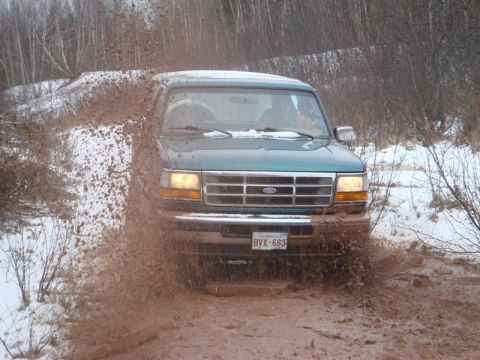 1996 Ford Bronco - A green 1996 Ford Bronco navigates a muddy trail with snow on the ground.
