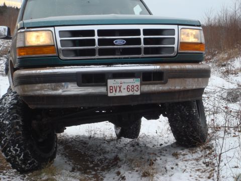 1996 Ford Bronco - Front view of a green Ford truck with a chrome grille and large tires, driving in a snowy landscape.