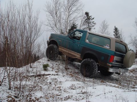 1996 Ford Bronco - A teal and black Ford Bronco navigates a snowy incline with its large off-road tires.