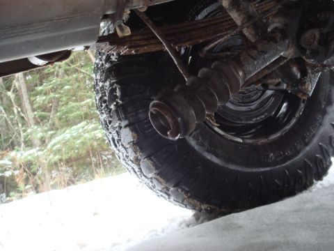1996 Ford Bronco - Undercarriage view of a vehicle's driveshaft boot and tire, with snow on the ground and trees in the background.