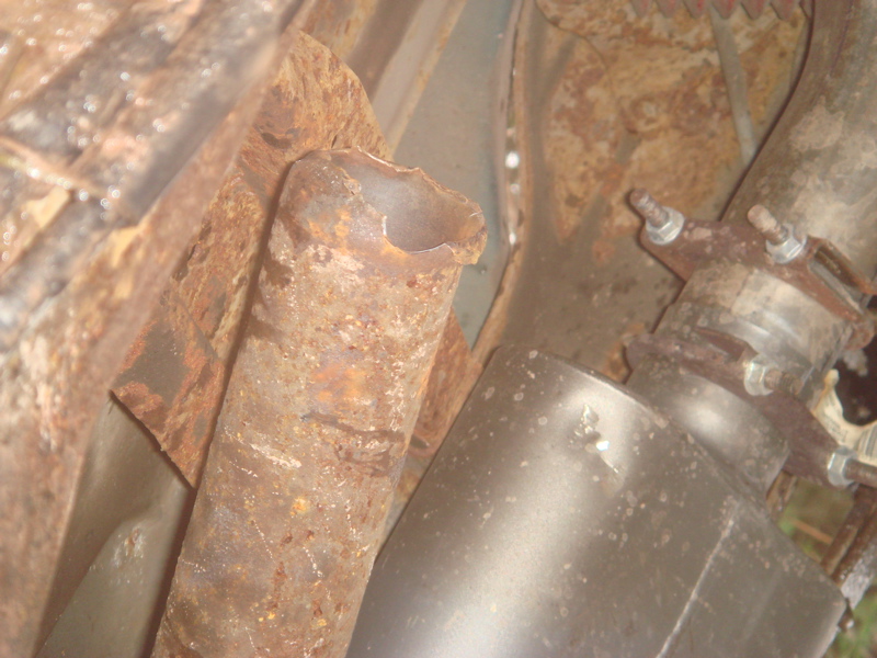 Rusted exhaust pipe broken off at jagged open end next to corroded frame and muffler