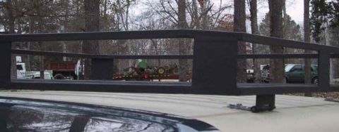 1995 Ford Bronco - A close-up of a black roof rack obscures a scene with multiple vehicles and trailers in a wooded area.