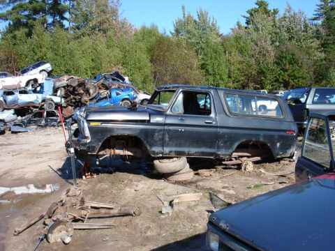 1996 Ford Bronco - This black SUV, likely a 1978 model, sits on stacked tires in a junkyard with its wheels removed.