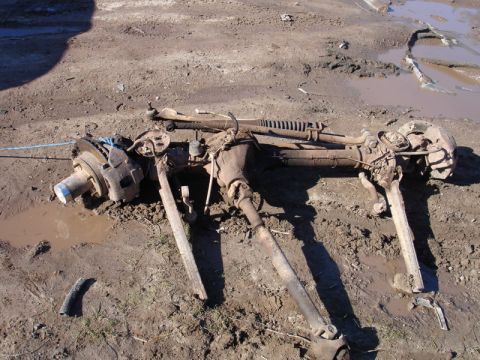 1996 Ford Bronco - Front axle assembly, likely from a truck or SUV, disassembled and resting on muddy terrain.