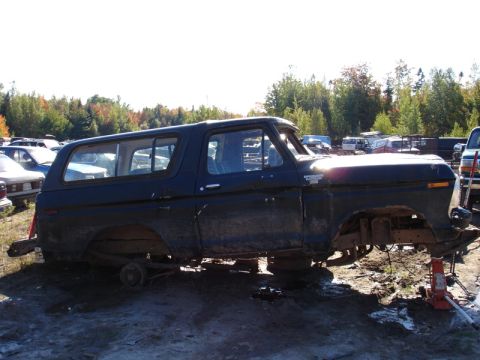 1996 Ford Bronco - A dark-colored Ford Bronco body sits on an orange jack in a junkyard with other vehicles visible.
