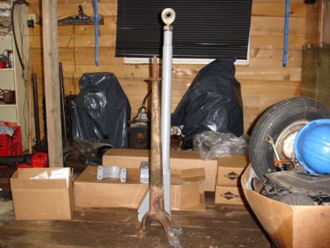 1996 Ford Bronco - A metal component, possibly a steering or suspension part, is shown in a workshop with various boxes and covered items in the background.
