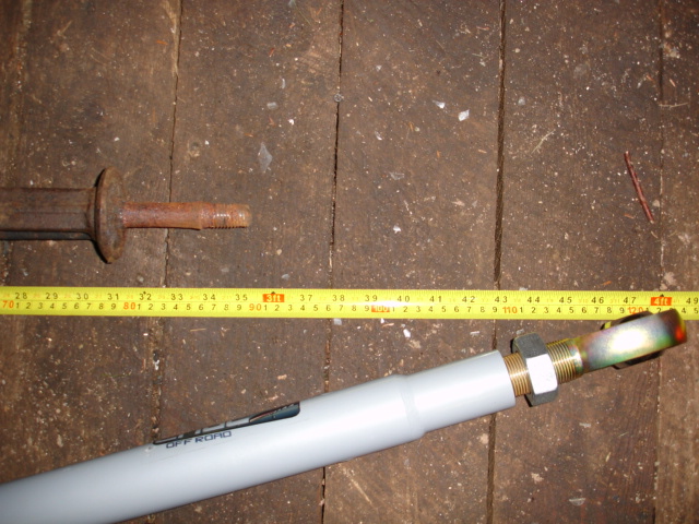 Rusty metal rod and white pipe with 'OFF ROAD' text, measured by a yellow tape measure on wooden planks
