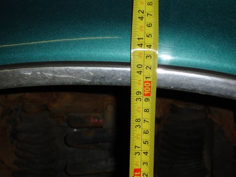 1996 Ford Bronco - A yellow measuring tape is used to measure the clearance above a vehicle's tire.