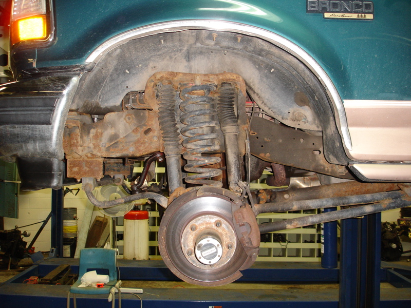 1996 Ford Bronco rear suspension showing rust on the frame and wheel well. The vehicle is on a lift
