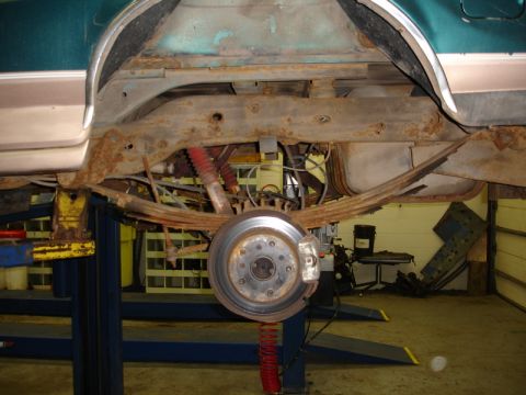 1996 Ford Bronco - The heavily rusted underbody of a vehicle is shown while on a lift, revealing its suspension components.