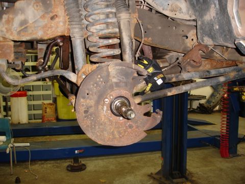 1996 Ford Bronco - Close-up of a vehicle's rusty brake rotor and suspension system, undergoing maintenance on a lift.