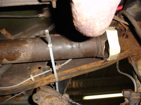1996 Ford Bronco - Close-up view of a vehicle's driveshaft and exhaust pipe, showing some rust and temporary repairs.