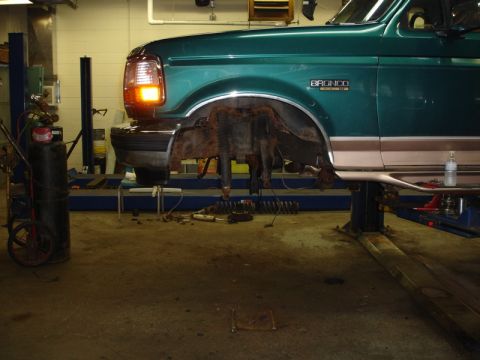 1996 Ford Bronco - The front suspension of a 1996 Ford Bronco is being worked on in a garage, with parts laid out on the floor.