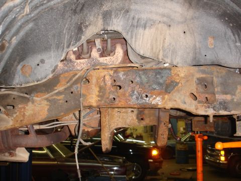 1996 Ford Bronco - The heavily rusted frame of a vehicle is shown, with other cars in the background.