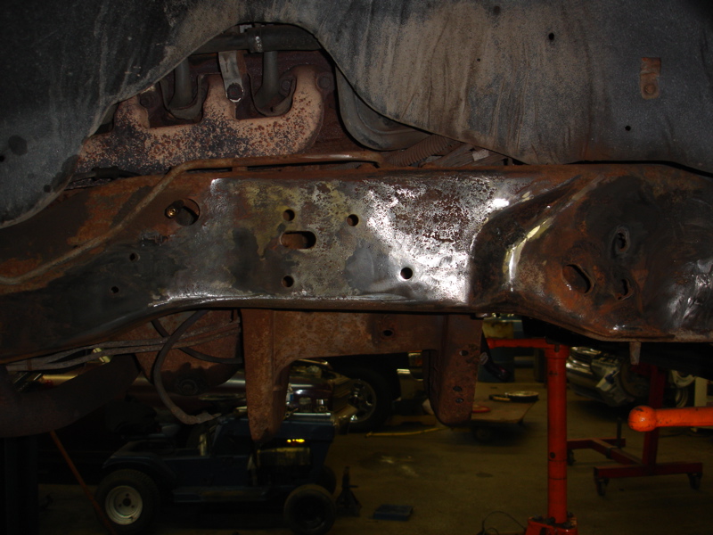 Rusty vehicle frame with exhaust manifold and suspension components visible