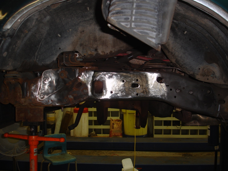 Underside view of a vehicle frame being repaired, showing rust and new welds