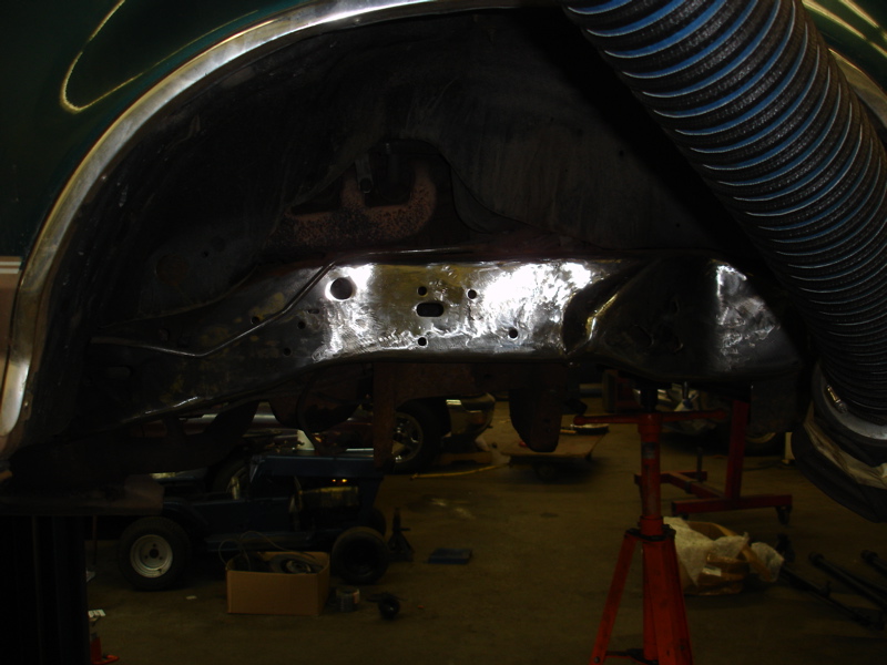 Underside of a vehicle showing frame rails, suspension, and part of the wheel well. A large hose is visible at the top right