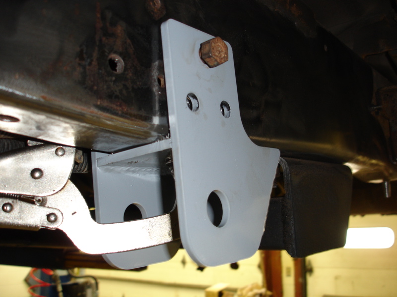 Close-up of a gray metal bracket bolted to a vehicle's rusty frame, with a vise grip holding a piece of metal