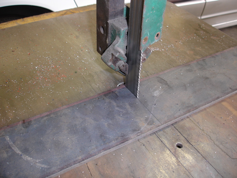 Bandsaw cutting a flat metal bar on a workbench. Metal shavings are visible on the surface