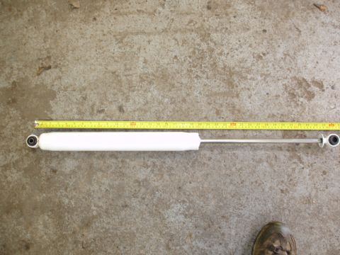 1996 Ford Bronco - A white shock absorber is laid out horizontally and measured with a yellow tape measure on a concrete surface.