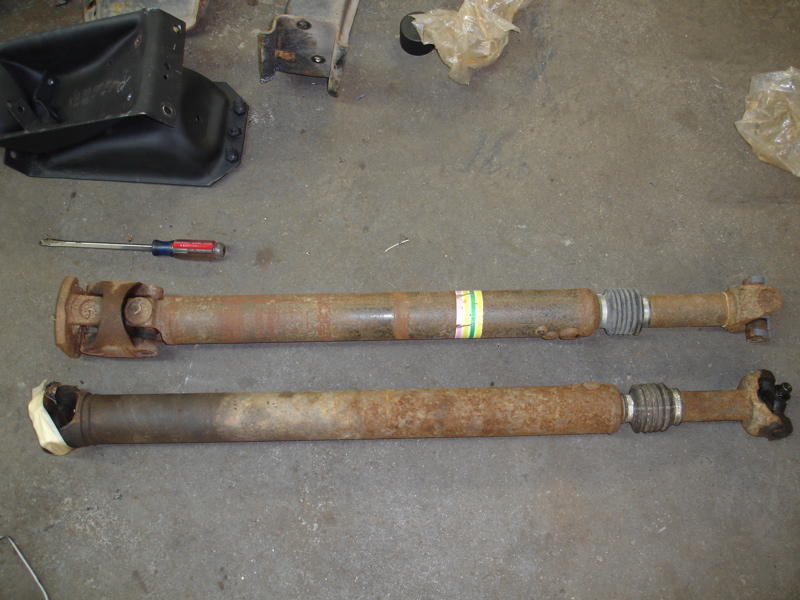 Two rusty driveshafts on a concrete floor, one with a yellow and green label