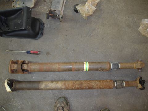 1996 Ford Bronco - Two driveshafts are shown on a concrete floor next to a screwdriver, with other vehicle parts in the background.