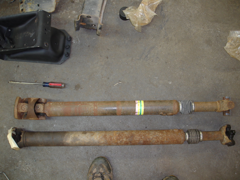 Two rusty driveshafts laid out on a concrete floor with a screwdriver