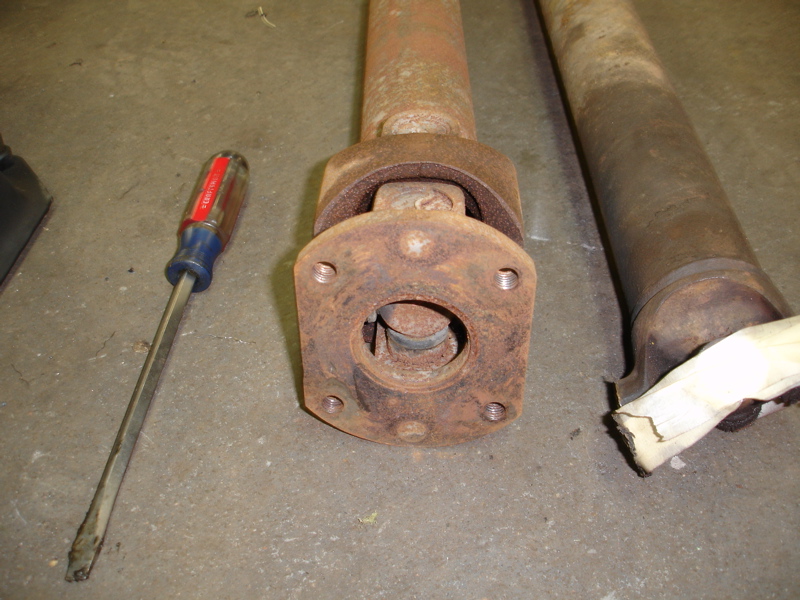 Two rusty driveshafts and a flathead screwdriver on a concrete floor