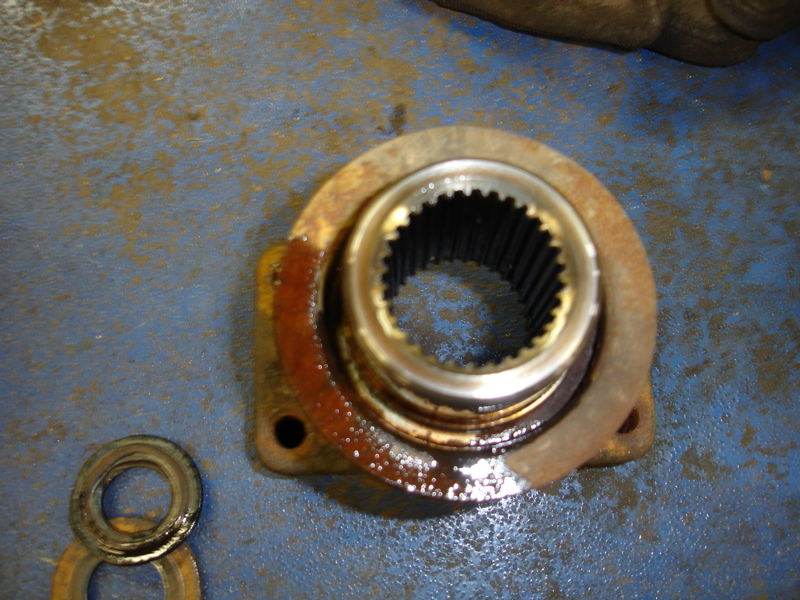 Rusted metal flange with internal splines and two washers on a blue surface