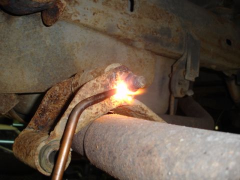 1996 Ford Bronco - A torch is used to cut a rusted bolt on a vehicle's undercarriage, likely during a repair or modification.
