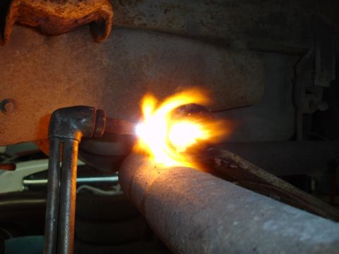 1996 Ford Bronco - A close-up view of an exhaust pipe being cut with a torch.