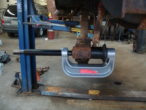 1996 Ford Bronco - A C-clamp tool is used to compress a suspension component on a vehicle in a repair shop.