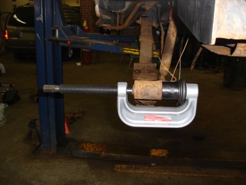 1996 Ford Bronco - A mechanic uses a C-clamp tool to press a suspension bushing on a vehicle in a garage.