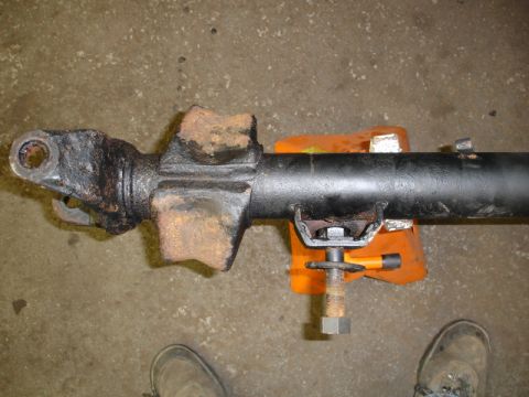 1996 Ford Bronco - A close-up view of a vehicle's driveshaft, held by an orange jack stand, with visible rust and wear.