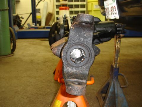 1996 Ford Bronco - A rusty suspension component is supported by jack stands in a garage setting.