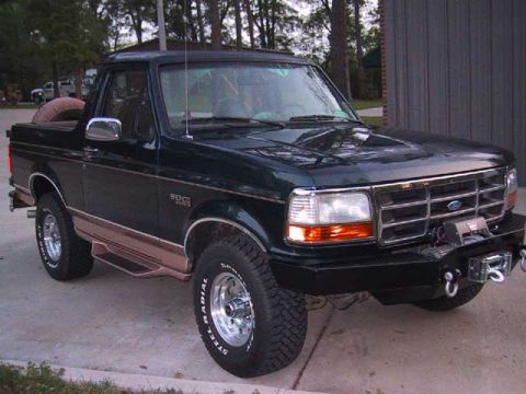 1995 Ford Bronco - This Ford Bronco is parked outside a building with trees in the background.