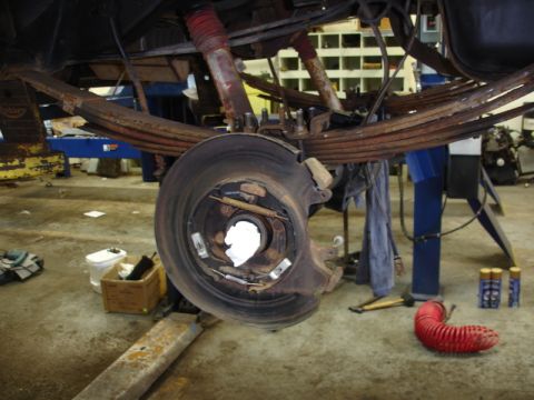 1996 Ford Bronco - Close-up view of a vehicle's rear suspension and brake assembly, showing leaf springs and red shock absorbers.