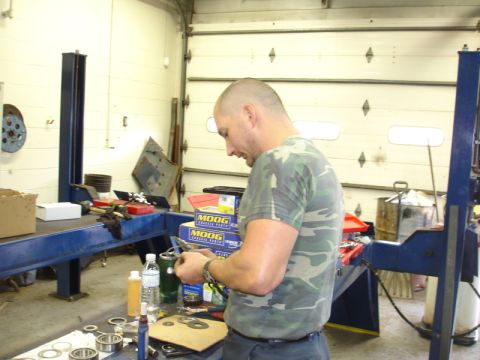 1996 Ford Bronco - A mechanic works on vehicle parts in a garage, with boxes of MOOG components visible.