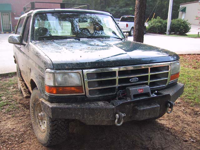 Muddy dark green Ford Bronco with black winch bumper and Warn winch, front three-quarter view