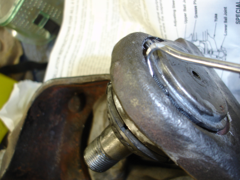 Close-up of a ball joint being serviced with a tool, diagram in background