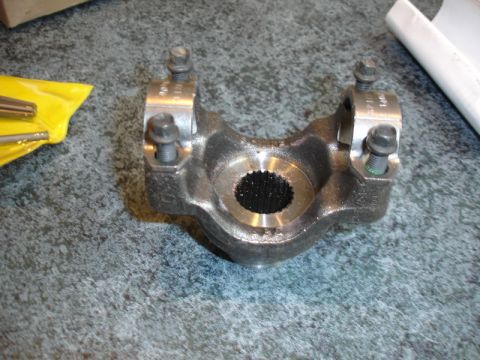 1996 Ford Bronco - A metal driveshaft yoke with a splined opening sits on a speckled surface next to a yellow packet of tools.