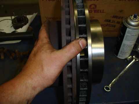 1996 Ford Bronco - A hand holds a brake rotor, with a can of lubricant and a wrench visible in the background.