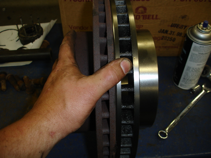 hand holding a brake rotor, with a can of spray lubricant and a wrench on the table