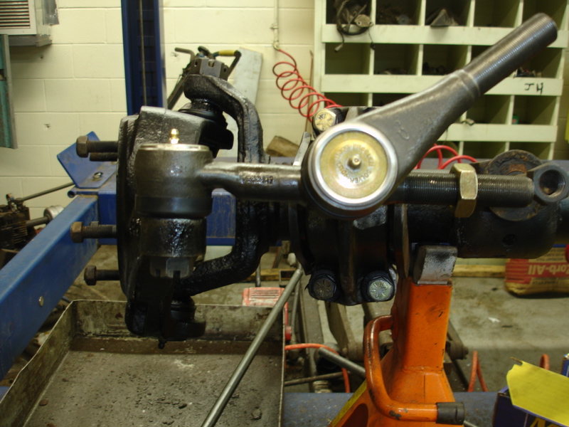 Close-up of vehicle steering linkage and suspension parts, including tie rod ends and ball joints, on an orange jack stand