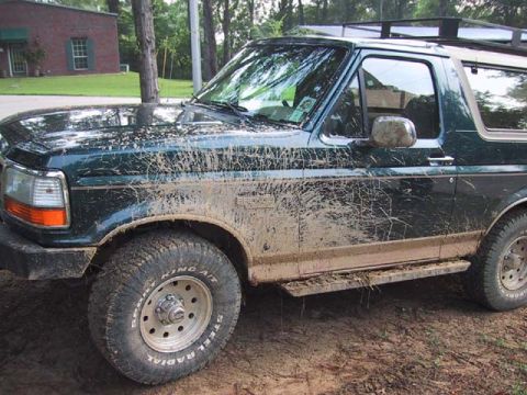 1995 Ford Bronco - A mud-covered Ford Bronco is seen from the side, with its front fender, door, and running board heavily soiled.