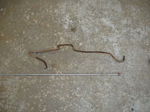 1996 Ford Bronco - A rusted metal bracket and a metal rod are shown on a concrete surface.