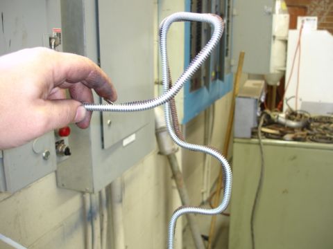 1996 Ford Bronco - A hand manipulates a piece of flexible metal conduit in front of industrial electrical panels.