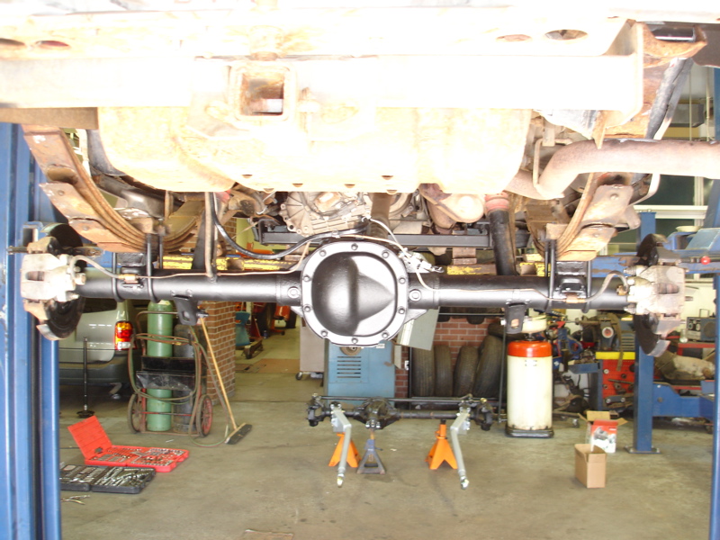 Underside view of a vehicle's rear axle assembly on jack stands in a garage