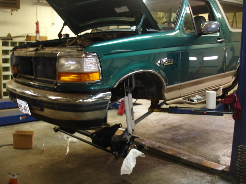 Green 1996 Ford Bronco with hood open, front end on lift, chrome bumper, tan trim