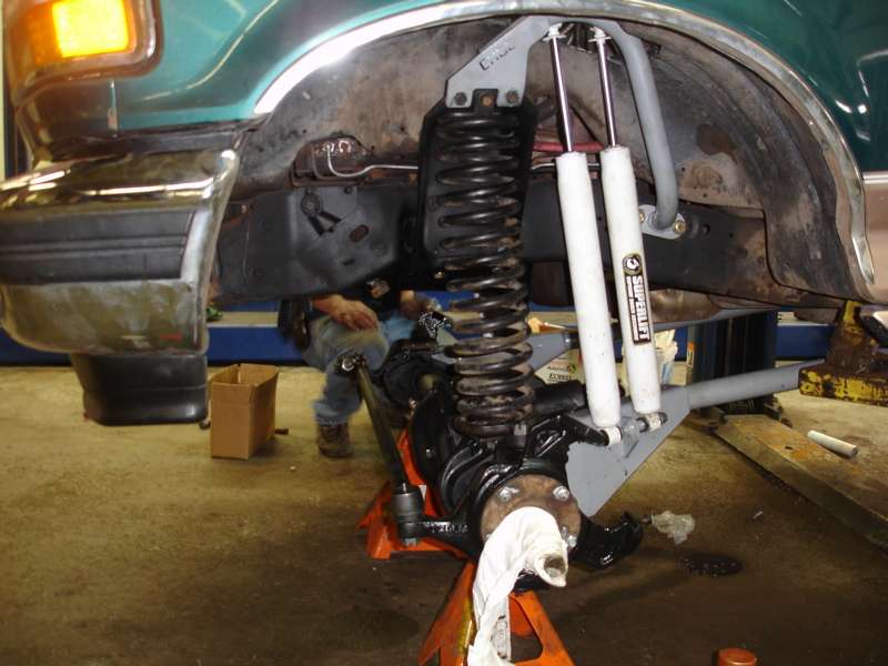 close-up of vehicle's front suspension with new shocks and springs installed, mechanic visible in background